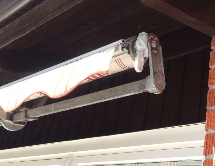 Terrassmarkis delvis utrullad med synlig mekanism och vev under takkant nära husvägg.