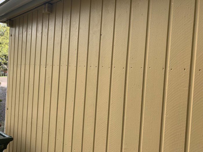 Gulmålad vertikal träpanel på ett garage byggt 1975, eventuellt tunnare än standard 21x120 baspanel.
