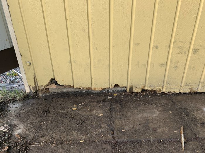 Skadad gul garagepanel med behov av byte, synlig träskada vid nederkanten.