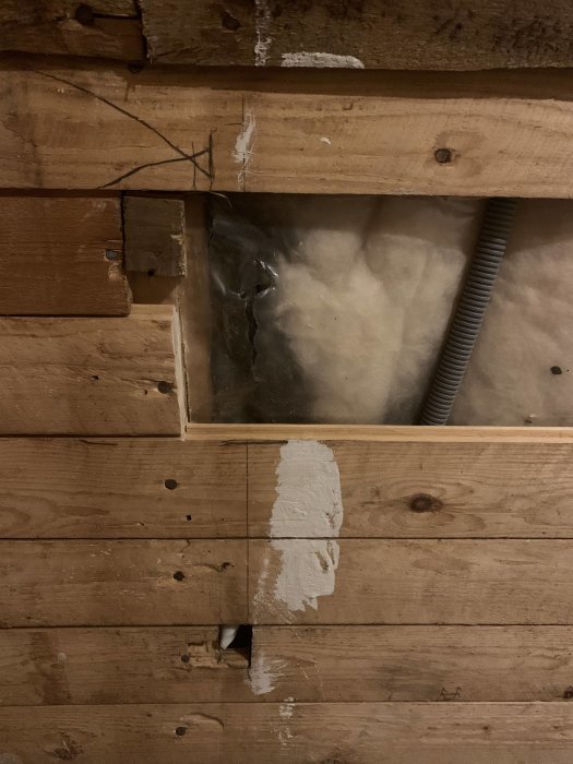 Inblick under innertaket med träbalkar, vit sprucken plast och svart isolering, tecken på möjlig fuktskada.