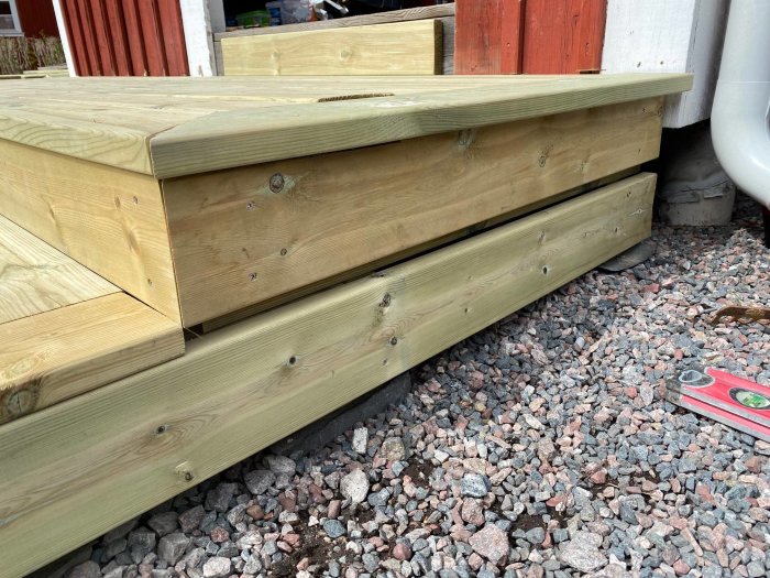 Hörn av en trätrall med ett synligt mellanrum mellan brädorna och sidan, mot en grusig mark.