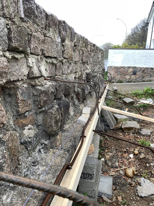 Förberedelse för gjutning av betongkant längs en stenmur med brädor och armeringsjärn.