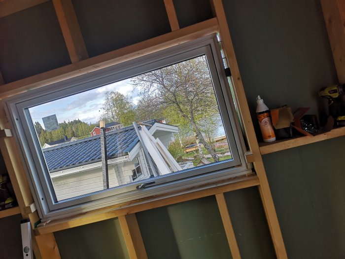 Nymonterat fönster med utsikt över tak och träd, verktyg och monteringsmaterial synligt.
