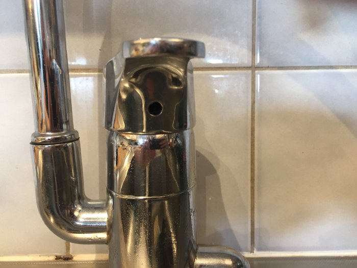 Närbild av en kromad köksblandare med en synlig insex-skruv, mot en kakelväggsbakgrund.