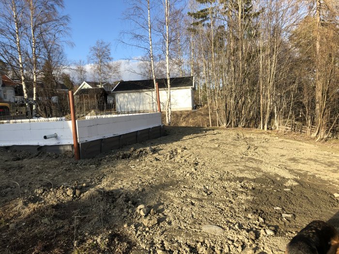 Grundarbete för hus med tre uppförda sidoväggar, öppning för källarnedgång, i förortsområde.