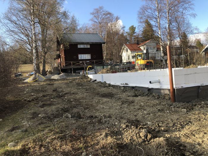 En byggarbetsplats med tre uppförda vita isoleringsväggar i förgrunden, i en trädgård med husbakgrund.