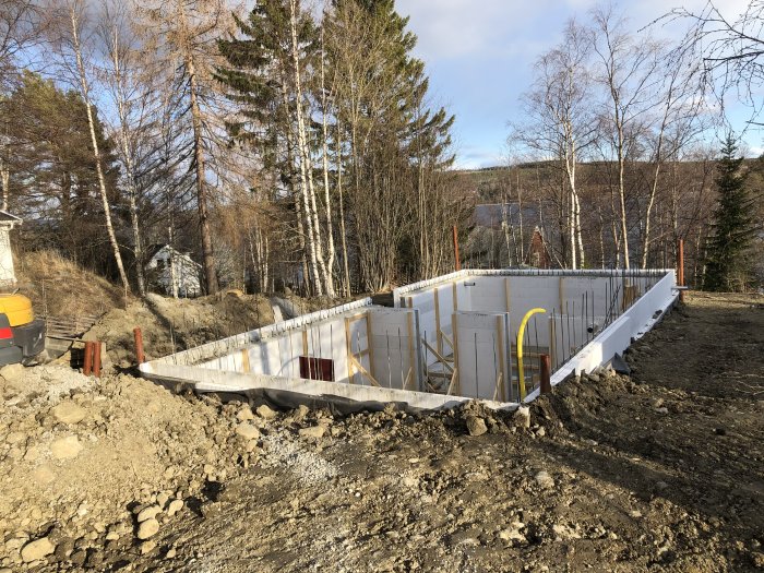 Grundkonstruktion med tre färdiga sidor av isolerade betongformar för ett byggprojekt, plats för källarnedgång synlig.
