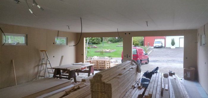 Nyinstallerade väggskivor i ett garage under renovering med trävirke, verktyg och en röd skåpbil synlig genom öppningen.