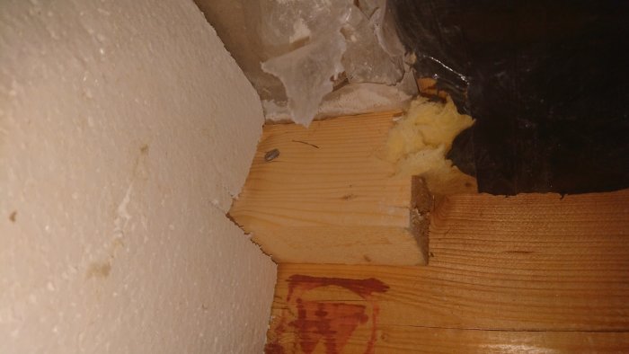 Upprivet hål i spånskiva under badrumsgolv, isolering och bit av gipsskiva syns.