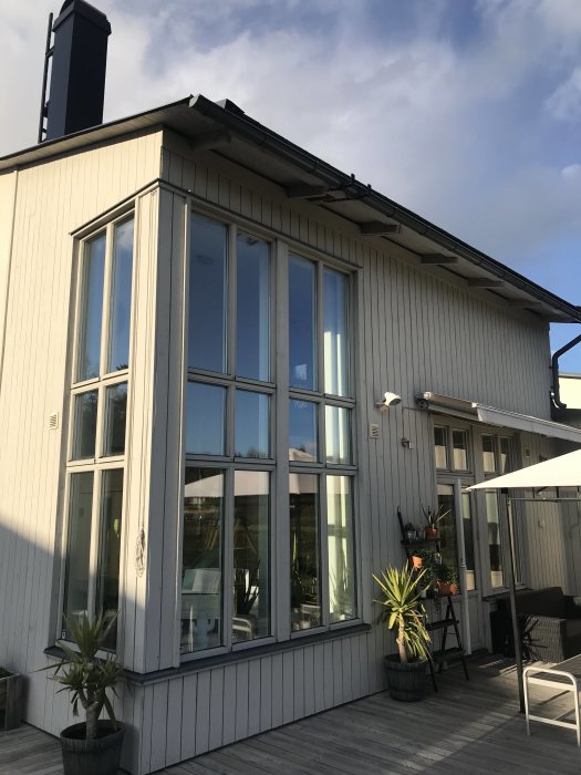 Vit träfasad hus med stegjärn monterade på takkanten ovanför ett fönsterparti och terrass.