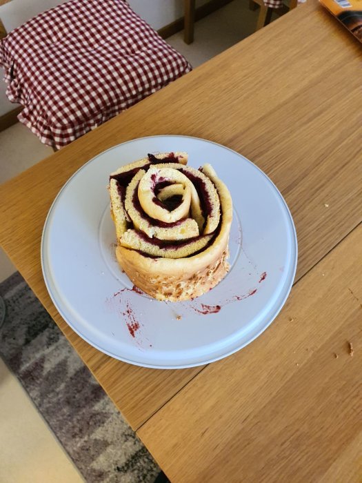 Hemlagad spiralformad tårta med jordgubbsfyllning, grädde och hallon, med röd dekorationsgel och synlig skada.