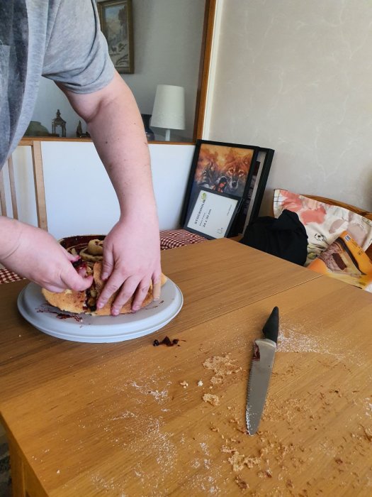 Person som serverar tårta med jordgubbar och hallon, brödsmulor och kniv på bordet.