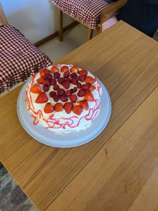 Hemgjord tårta med grädde och bär, röd dekorationsgel och synlig skada på kanten.