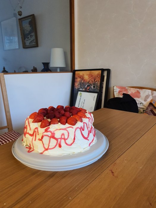 Hemgjord tårta med grädde och jordgubbar, dekorerad med röd gel, på ett köksbord.