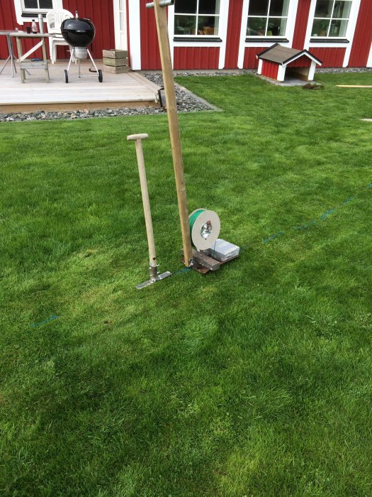 Egenbyggd kabelplog med läggarrör svetsat under en skyffel, på en gräsmatta.