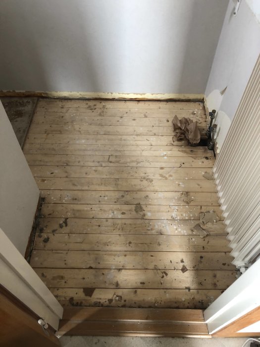 Upprivet golv i gästtoalett med synliga träplankor och en radiator vid väggen inför renovering för golvvärme.