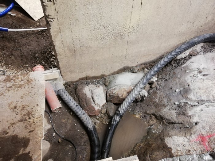 Nybyggda stödmurar med dräneringsrör och en grusramp vid en byggplats.