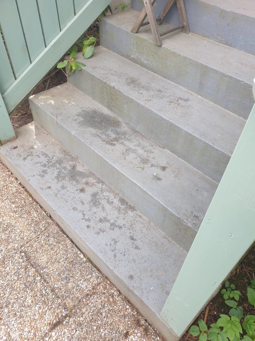 Betongtrappa utomhus med fyra steg, mindre slitage och grönt räcke.