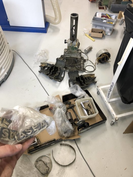 Nedmonterad Asea LLB-1 pelarborr i delar spridda på golvet, en hand håller en del i plastpåse.