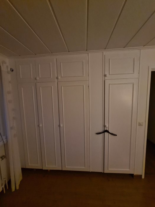 Gammaldags vita garderober med ojämn stängning och synliga slitage i ett sovrum.