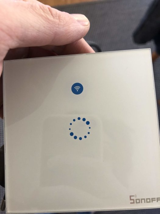 Hand håller en smart väggbrytare med Wi-Fi-symbol och statusindikator, märkt "Sonoff".