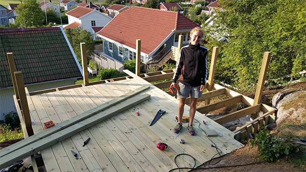 Person står på en pågående altanbygge med verktyg och byggmaterial runtomkring.
