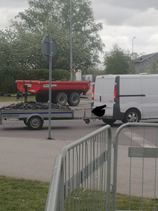 Hantverkarbil med släp lastat med materialsäckar nära trottoarkant, säckarna verkar rörliga under färd.