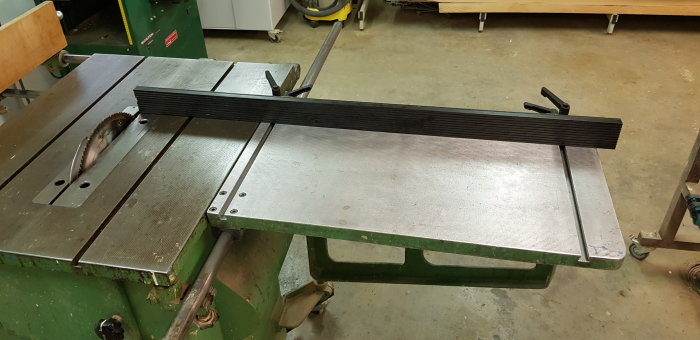 Ett justerbart sågbord i en verkstad med en synlig sågklinga och en nyligen justerad anhåll i aluminium.