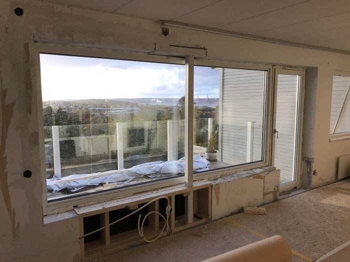 Renoverat rum med stort nyinstallerat fönster, altandörr och stödstolpe i konstruktionen, utsikt mot natur.