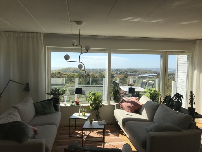 Renoverat vardagsrum med stora fönster, altandörr, soffor och utsikt över landskap.