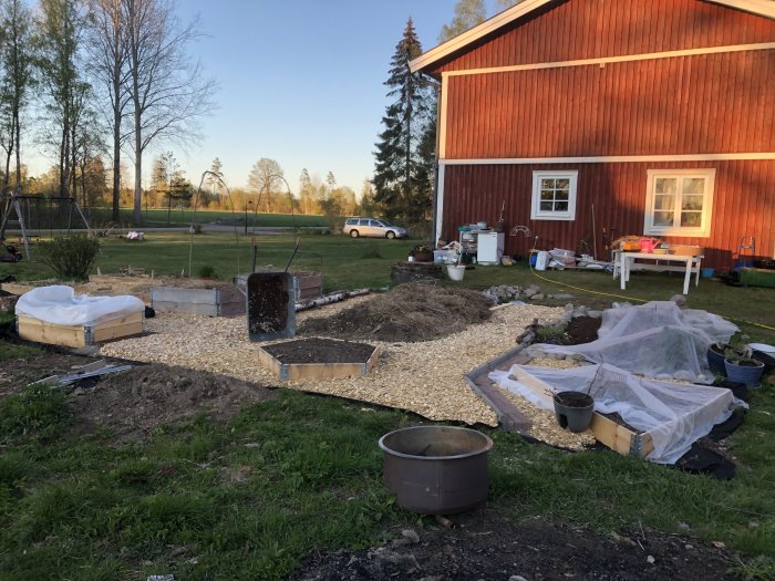 Trädgårdsprojekt med en nybyggd odlingslåda, spaljé och plattor vid en röd stuga i kvällssol.