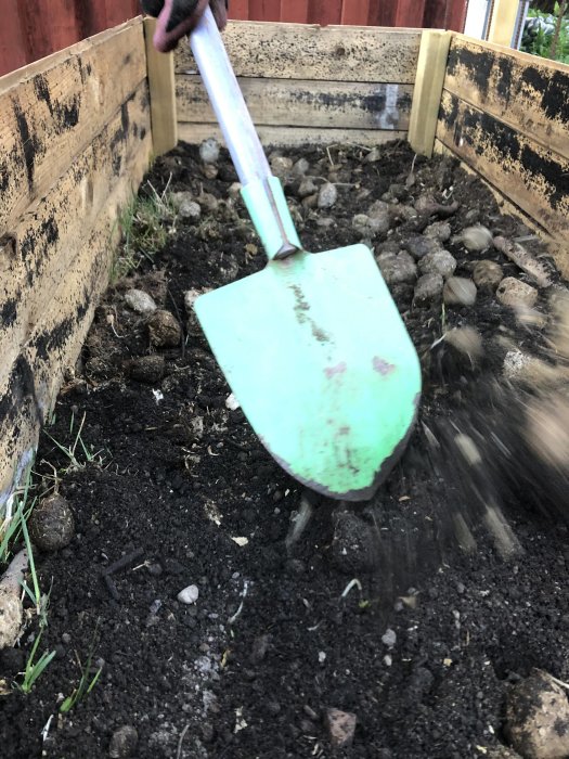 Bild av en spade som förbereder jord i en nyanlagd odlingslåda med blandad jord och material.