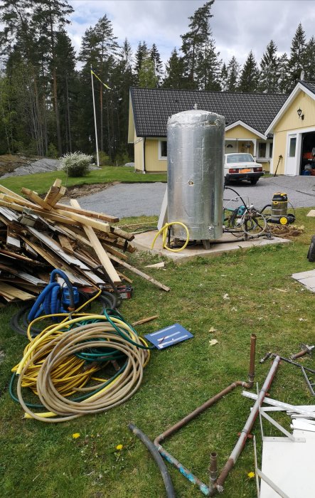 Ett gammalt pumphus framför ett hus med byggmaterial och verktyg utspridda på marken.