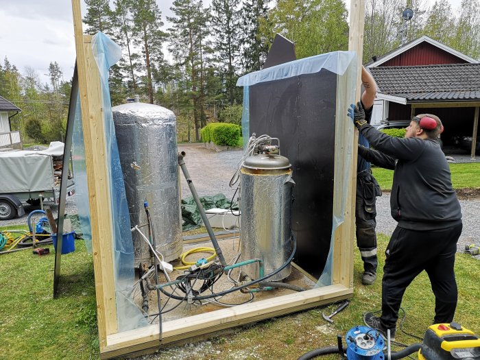 Bygge av nytt pumphus med personer som arbetar, isolering synlig, trästomme och verktyg omkring.