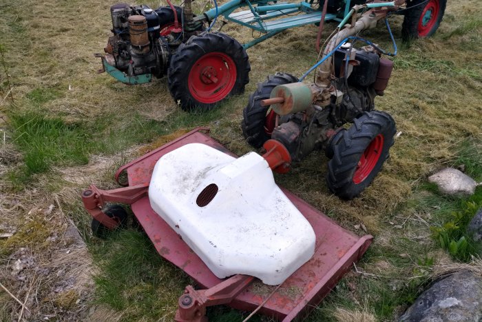 Ett klippdäck med nybytta remmar bredvid en röd traktor på en gräsmark.