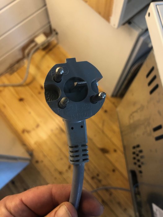Elektrisk sladd med blå stickpropp hålls framför ett uttag, synliga skruvkontakter och märkning.