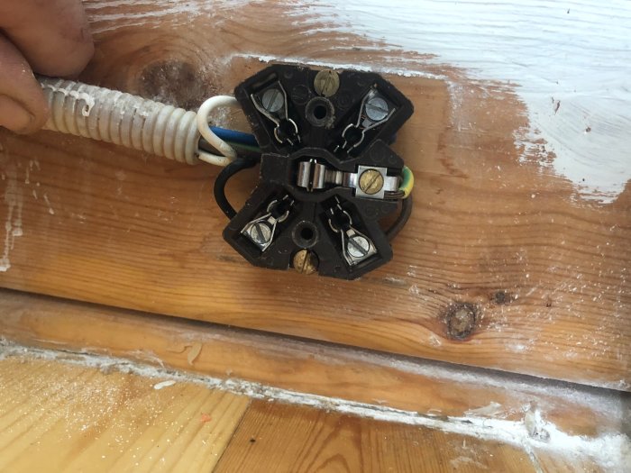 En öppen elektrisk uttag med ansluten vit kabel på ett trägolv, hand syns hålla i kabeln.