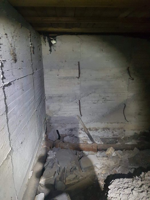 Oupptäckt källarrum med betongväggar och rörmokarens material på golvet.