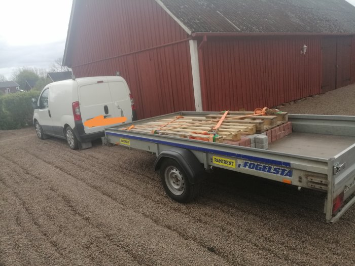 Lastbil med släp lastat med pallar och stenplattor säkrade för transport.