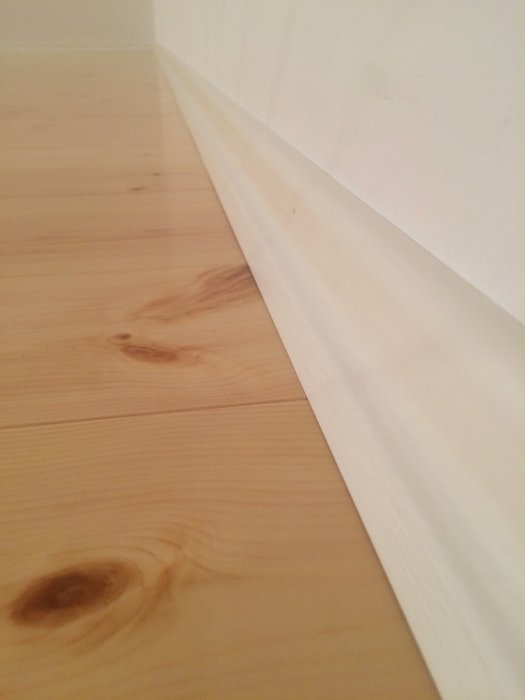 Ett hörn av ett rum med BASECO furugolv och en vit fotlist, golvet har fin ådring och minimala springor.