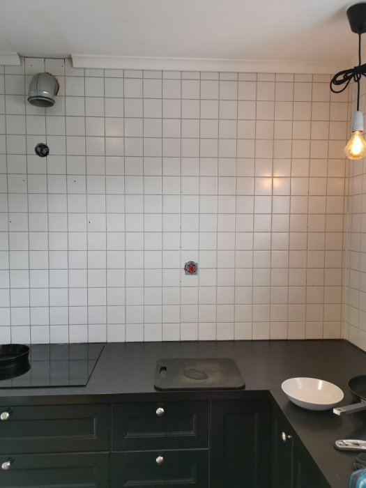 Kök med vägg kaklad i vitt 10x10 kakel, utan fläkt och förberett för renovering.