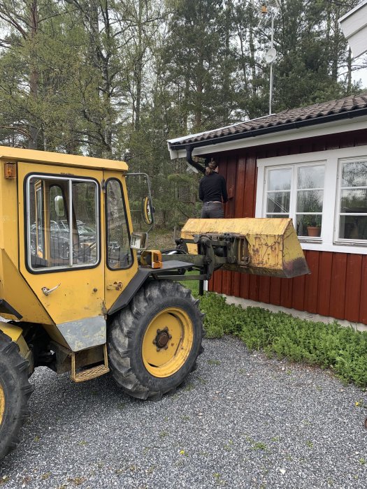 Person målar fasaden på ett rött hus med hjälp av en gul mobil arbetsplattform.