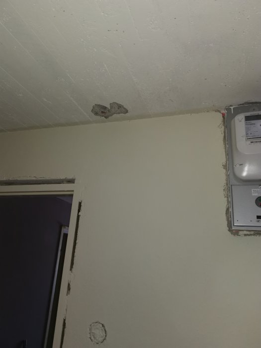 Vägg med färska borrade hål nära elcentral, ett halvfärdigt hål där kabel syns.