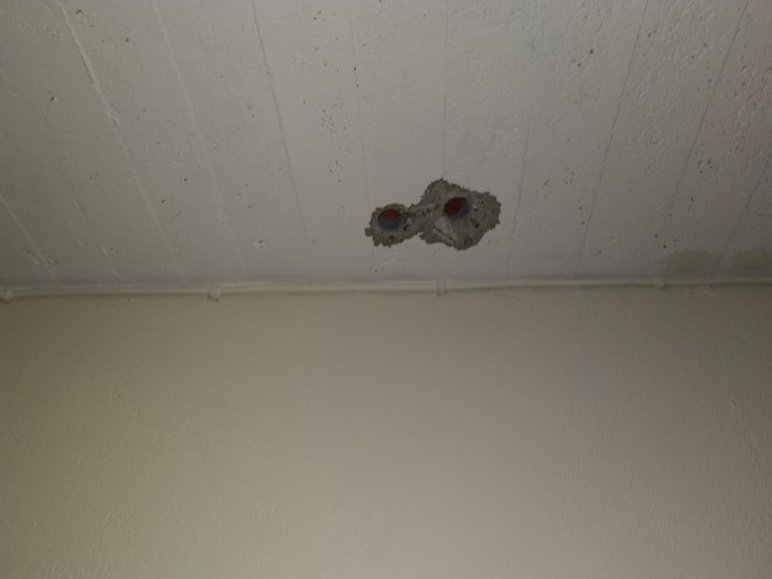Hål borrade i vit takyta med synliga rör och kablar, skador efter borrning nära elinstallationer.