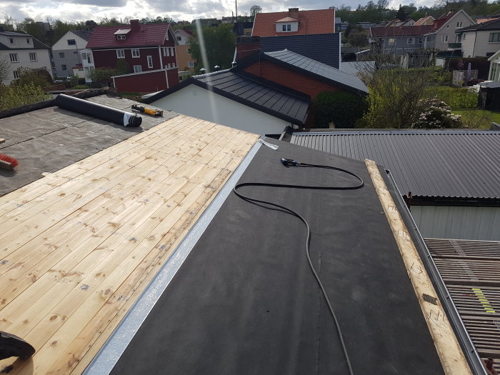 Nytt träsponttak under installation bredvid befintligt svart tak, i ett bostadsområde.