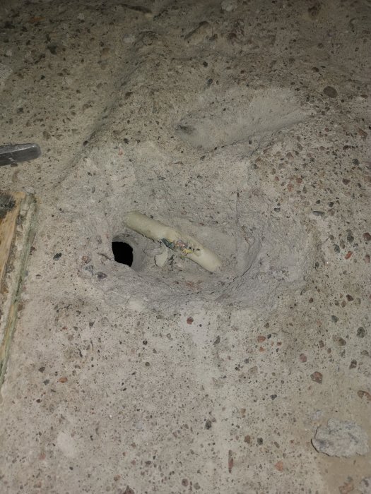 Ett hål i betong med ett plastavloppsrör omringat av lite skräp, innan omvik läggs för att skydda röret.