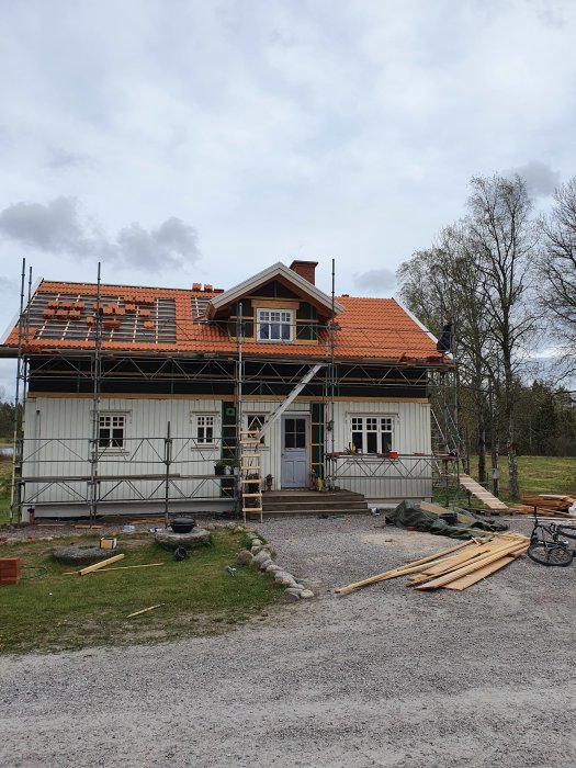 Hus under renovering med pågående takarbete och omläggning av takpannor, ställningar runt byggnaden.