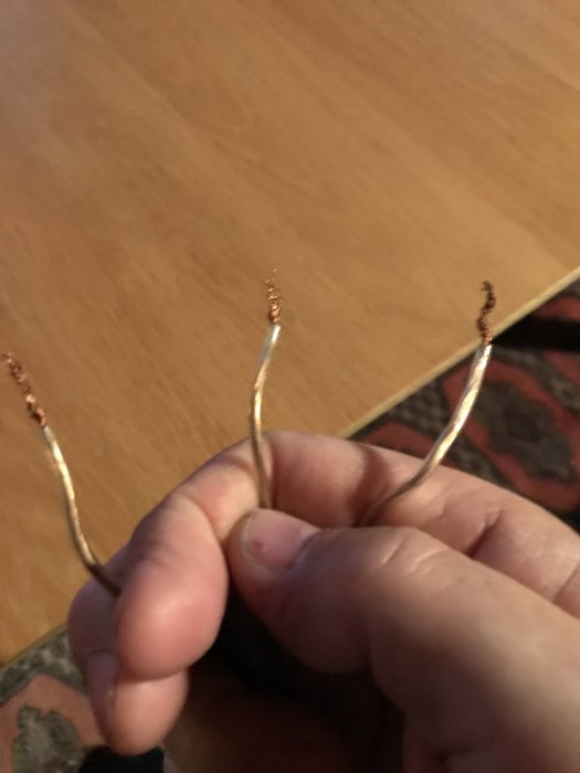 Hand som håller tre avskalade elektriska ledningar.