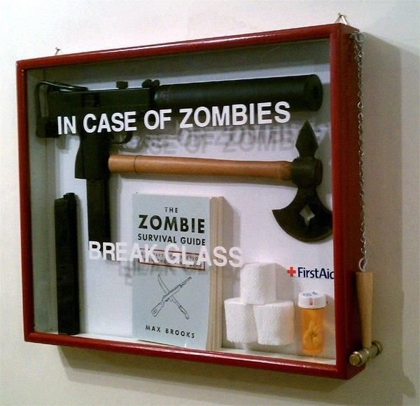 Ett skämtsamt zombieöverlevnadskit med bl.a. en bok, yxa och första hjälpen-utrustning, monterat i ett rött väggskåp.