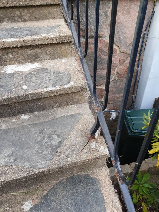 Sprucken betongtrappa med svart staket, behöver reparation.